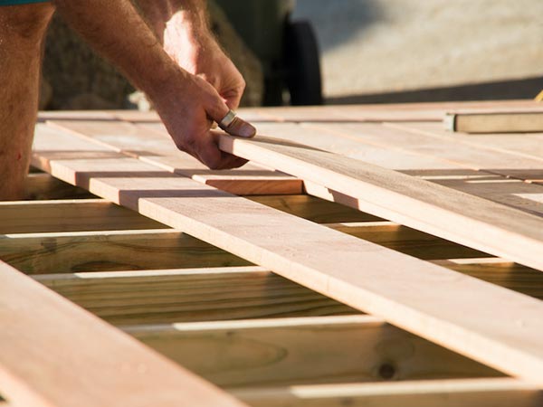 Close-up of hands hammering a nail into wooden floor joists during construction.