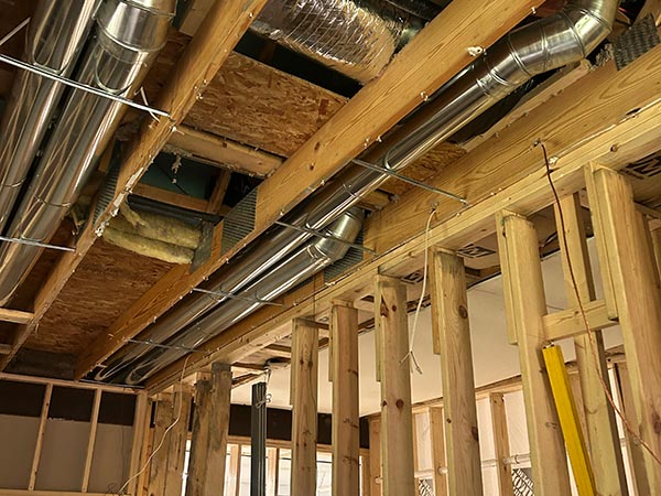 Interior of a building under construction with exposed wooden studs and shiny metal HVAC ducts running along the ceiling